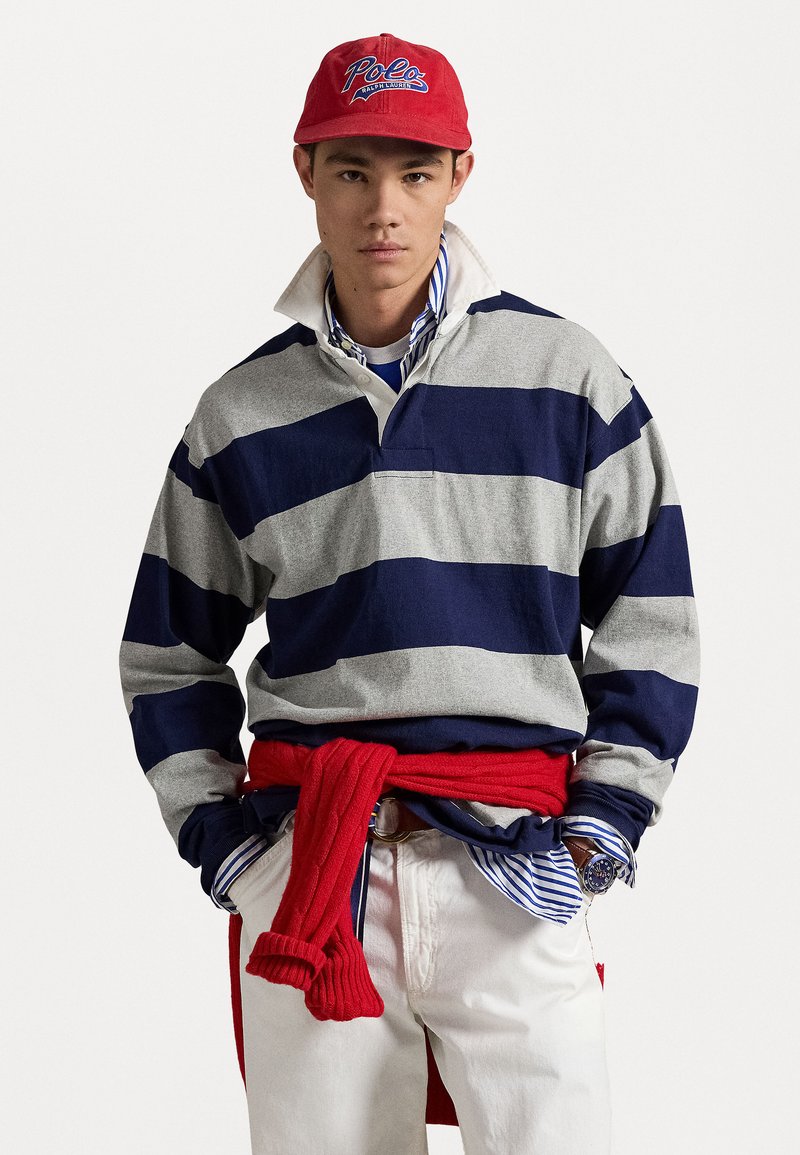 Rugby-style shirt in gray and navy stripes, with a white collar. Red sweater tied at the waist. Light-colored pants and striped shirt underneath.
