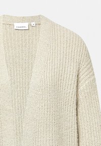 Lichtbeige gebreide cardigan met een V-halsontwerp, losse pasvorm, gestructureerde stof en subtiele metalen accenten. Etiket zegt "COMMA" en maat 36.