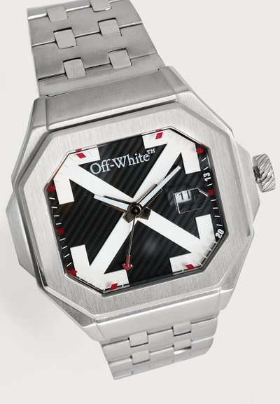 Montre-bracelet argentée blanc cassé, avec un bracelet métallique anguleux, un cadran noir, de grandes aiguilles blanches, des accents rouges et un affichage de la date.