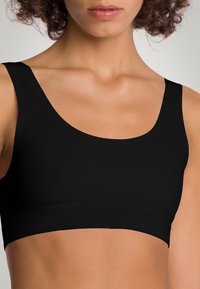 Top sportivo nero con una texture liscia e a coste, spalline larghe e una fascia senza cuciture in vita. Design minimalista, senza motivi aggiuntivi.
