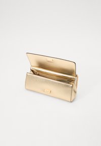 Porte-monnaie en métal doré avec une finition texturée, doté d'un compartiment zippé et d'une bandoulière en chaîne. S'ouvre pour révéler un intérieur spacieux.