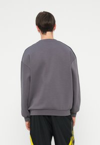Grå sweatshirt med avslappnad passform, ribbade muddar och nederkant, samt detaljer vid axelsömmarna. Texturerad tygkvalitet, minimalistisk design.