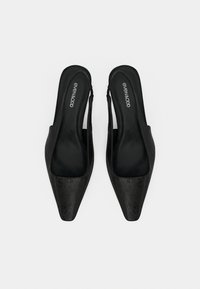 Μαύρα πέδιλα με λουράκι πίσω, μυτερή μύτη, υφασμένο επάνω μέρος και λεία εσωτερική επιφάνεια. Μινιμαλιστικός σχεδιασμός με κομψή σιλουέτα.