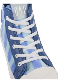 Tenisky s modrým kostkovaným vzorem mají kožený svršek, bílé šněrování a gumovou podrážku. Disponují texturovaným povrchem a logem na jazyku.