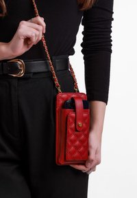 Červená kožená pouzdro na telefon s prošívaným vzorem, odnímatelným řetízkovým popruhem, předním zapínáním na knoflík a slotem pro smartphone.