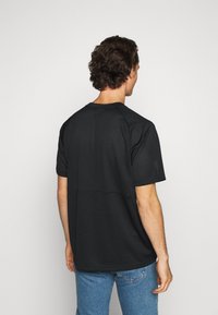 Svart t-shirt med kort ärm som har en perforerad mesh-design, mjuk textur och rak fåll, bärs med ljusblå denimjeans.