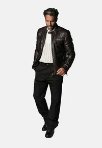 Veste en cuir marron avec épaules matelassées, pull en maille torsadée blanche, pantalon noir et chaussures noires ; coupe décontractée avec un design casual.