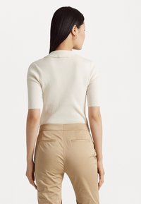 Ριγέ κρεμ μπλούζα κοντό μανίκι συνδυασμένη με εφαρμοστά μπεζ παντελόνια. Η μπλούζα διαθέτει κλασικό γιακά και λεία υφή.