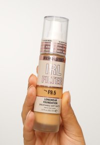 Base de maquillaje de larga duración en un envase transparente con dosificador. Presenta un tono bronceado etiquetado como "F9.5" y el texto "mate suave y transpirable" en un tono oscuro.