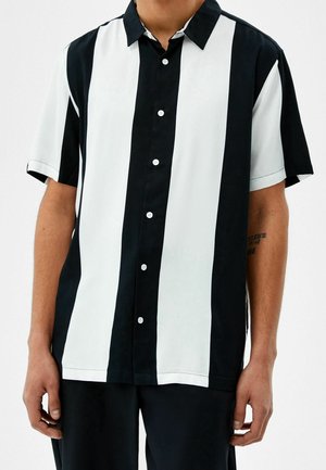 Camicetta a maniche corte con strisce verticali alternate nere e bianche, colletto a camicia e chiusura con bottoni frontale. Tessuto morbido.
