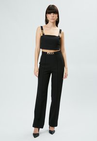 Top corto negro con tirantes gruesos y acentos de cadena dorada, combinado con pantalones negros de cintura alta que tienen un ajuste ceñido y una textura suave.