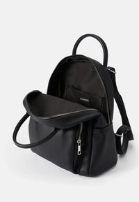 Mochila de couro preto com alças ajustáveis, compartimento principal com fecho e bolso frontal. O interior forrado apresenta uma etiqueta e textura suave.