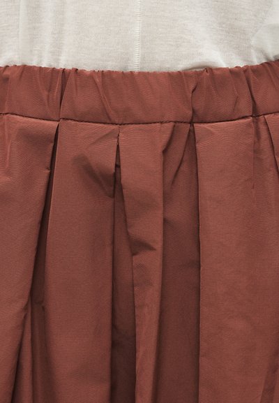 Φούστα σε καφέ σκουριά απόχρωση με ψηλή μέση, ευρείες πιέτες και ελαστική μέση, φορεμένη με ανοιχτό μπεζ τοπ με υφή.