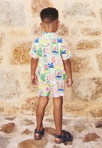 Kurzärmliger Overall in Pastellfarben mit verspielten Mustern von Pflanzen und Segelbooten. Hergestellt aus leichtem Stoff, verfügt über eine lockere Passform.