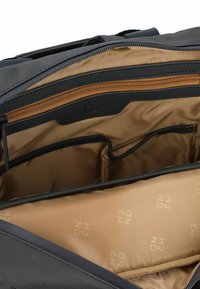 Interior de una bolsa de tela negra con un forro beige. Incluye un bolsillo con cremallera y múltiples compartimentos para la organización. Branding sutil "H2" visible.