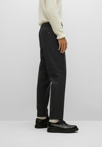 Pantalones negros ajustados con una cintura elástica, bolsillos laterales y un acabado elegante, combinados con zapatos negros con cordones.