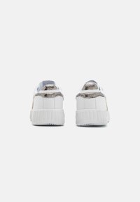 Baskets blanches avec des accents argentés texturés et une finition lisse. Vue arrière présentée montrant un talon rembourré et une semelle nervurée.