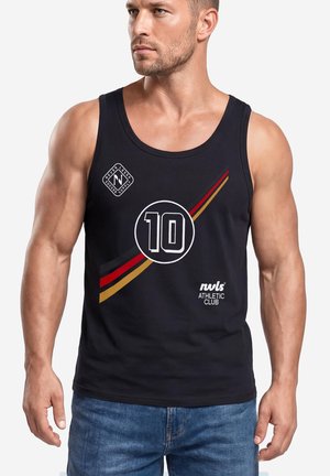 Sportlicher Mann trägt ein schwarzes Tanktop mit der Nummer 10 und bunten Streifen, kombiniert mit blauen Jeans, blickt nach links auf weißem Hintergrund.
