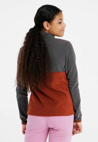 Veste en polaire avec une partie supérieure grise et une partie inférieure orange. Dotée d'un col haut et de manches longues. Texture douce, design ajusté.