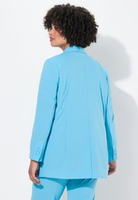 Un blazer azzurro chiaro su misura realizzato in un tessuto liscio, con una sola fessura sul retro e dettagli di bottoni sulle maniche.