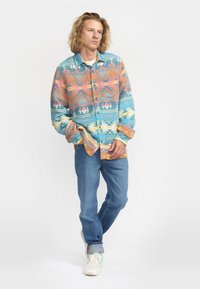 Gepersonaliseerde button-up shirt in pastelkleuren met geometrische ontwerpen; lange mouwen, puntige kraag, relaxte pasvorm. Draag het over een licht T-shirt en jeans.