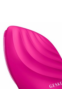 Brosse à cheveux en silicone rose avec une surface incurvée et nervurée et des poils fins. Présente un logo sur le côté, un design épuré et une texture lisse.