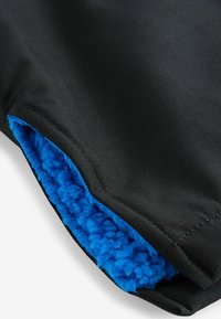 Svart tyg med en texturerad yta, med en blå fleecefoder synligt vid kanten. Designen betonar värme och komfort.