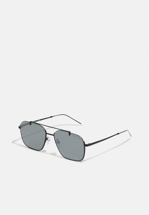 Lunettes de soleil noir en métal avec des verres gris, verres de forme ovale, plaquettes de nez ajustables et branches fines. Design minimaliste sans marque visible.
