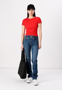 T-shirt rouge à rayures, jeans en denim bleus, baskets blanches, casquette noire et sac fourre-tout noir, présentés sur un fond neutre.