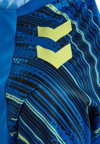 Blå idrottsshorts med ett vågigt svart och limegrönt mönster, prydda med två ljusgröna chevron-accenter på sidan. Slätt, lätt material.