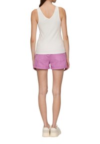 Weißes geripptes Tanktop mit V-Ausschnitt, kombiniert mit rosa Jeansshorts mit aufgerolltem Saum und hellen Plateausneakern.