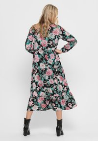 Maximein kukkia mustalla pohjalla, jossa on suuria vaaleanpunaisia ja teal-värisiä kukkakuoseja, pitkät hihat ja liehuva helma, yhdistetty mustiin nilkkabootseihin.