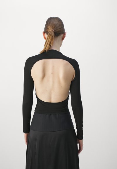 Black long-sleeve top featuring an open back design, with a fitted lower section and smooth texture, paired with a sleek black skirt.