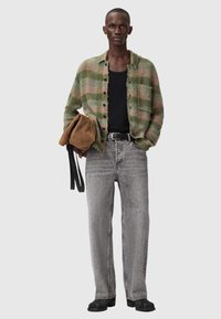 Πράσινη και ροζ καρό ζακέτα, μαύρο αμάνικο τοπ, γκρι τζιν και μαύρα παπούτσια. Το μοντέλο κρατά ένα καφέ τσάντα· παρουσιάζεται σε ουδέτερο φόντο.