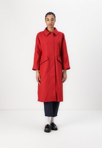 Czerwony płaszcz z kołnierzem, dwoma przednimi kieszeniami i ozdobnymi guzikami po bokach. Noszony na ciemnych spodniach i czarnych mokasynach, do tego białe skarpetki.