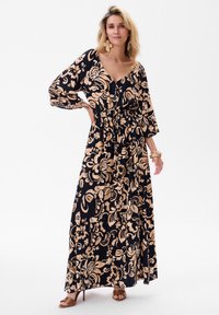 Maxi sukienka w granatowym kolorze z kwiatowym wzorem w jasnym beżu. Posiada długie rękawy, głęboki dekolt w kształcie V, ściągniętą w talii i zwiewny dół.