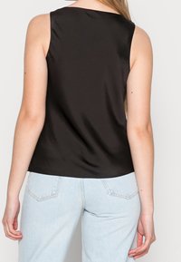 Top senza maniche in satin nero con una texture liscia, scollatura rotonda e vestibilità rilassata, abbinato a jeans a vita alta blu chiaro.
