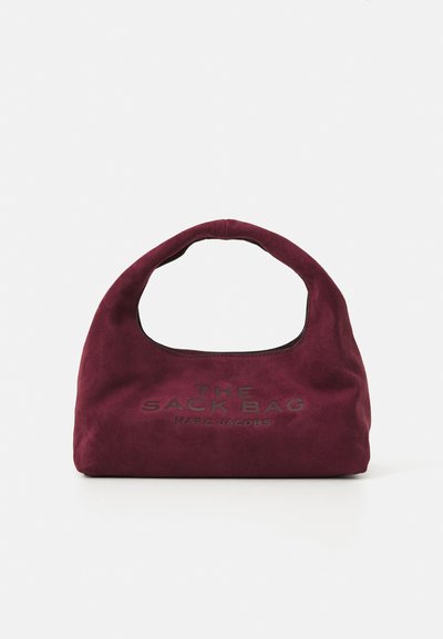 Petit sac à main en daim bordeaux avec une poignée courbée, "THE SACK BAG MARC JACOBS" embossé sur le devant, sur fond blanc.