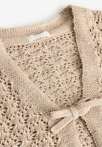 Beige strikket cardigan med blondecifre, prydet med små palietter og bindes foran. Blød tekstur og åben vævning.