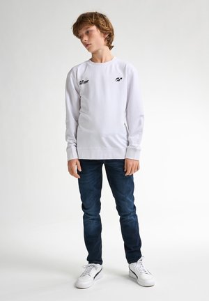 Sweat-shirt blanc à manches longues avec des impressions de logo noir, associé à un jean bleu foncé et des baskets blanches. Design simple et décontracté.