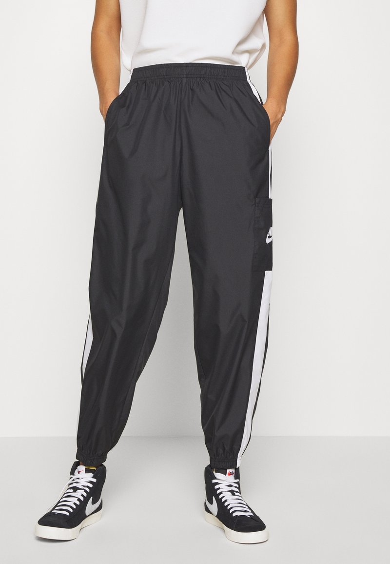 Black athletic jogger pants with an elastic waistband, white side stripes, and a cargo pocket. Styled with black high-top sneakers.