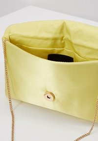 Žlutá saténová kabelka na ruku se zlatým zapínáním a texturovaným interiérem. Obsahuje zlatý řetízek pro snadné nošení.