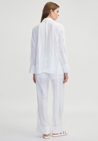 Witte, lichte, gestreepte stofset met een longsleeve shirt en wijde broek, met gedetailleerde accenten op de schouders.