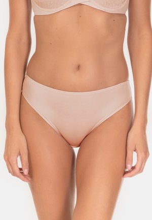 Kobieta w cielistym staniku i pasujących majtkach w stylu bikini, widoczny tors i górna część ud, stojąca na jednolitym tle.