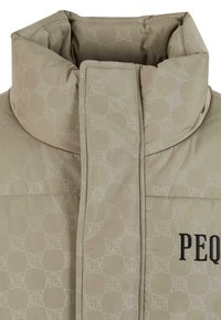 Polstret beige frakke med høj krave, der har et subtilt geometrisk mønster og sort "PEQUS" broderi på forsiden.
