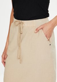 Jupe en lin beige dotée d'une taille à cordon, d'une poche latérale et d'une texture lisse. Le tissu semble léger et respirant.