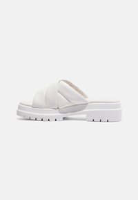 Witte slipper sandaal met dikke, gevoerde crisscross banden, een comfortabele zool en een gelijmde platformhak op een effen witte achtergrond.
