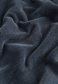 Material de catifea bleumarin cu pliuri moi și textură nervurată vizibilă, privit în prim-plan.