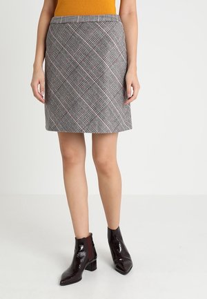 Karierter Rock in Grau mit rosa und schwarzen Akzenten, aus strukturiertem Stoff gefertigt. Besitzt eine taillierte Passform und endet über dem Knie. Kombiniert mit glänzenden schwarzen Knöchelstiefeln.