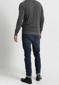 Maglione grigio con orlo a coste, abbinato a jeans blu scuro con risvolti e tasche posteriori. Stivali neri completano l'outfit.